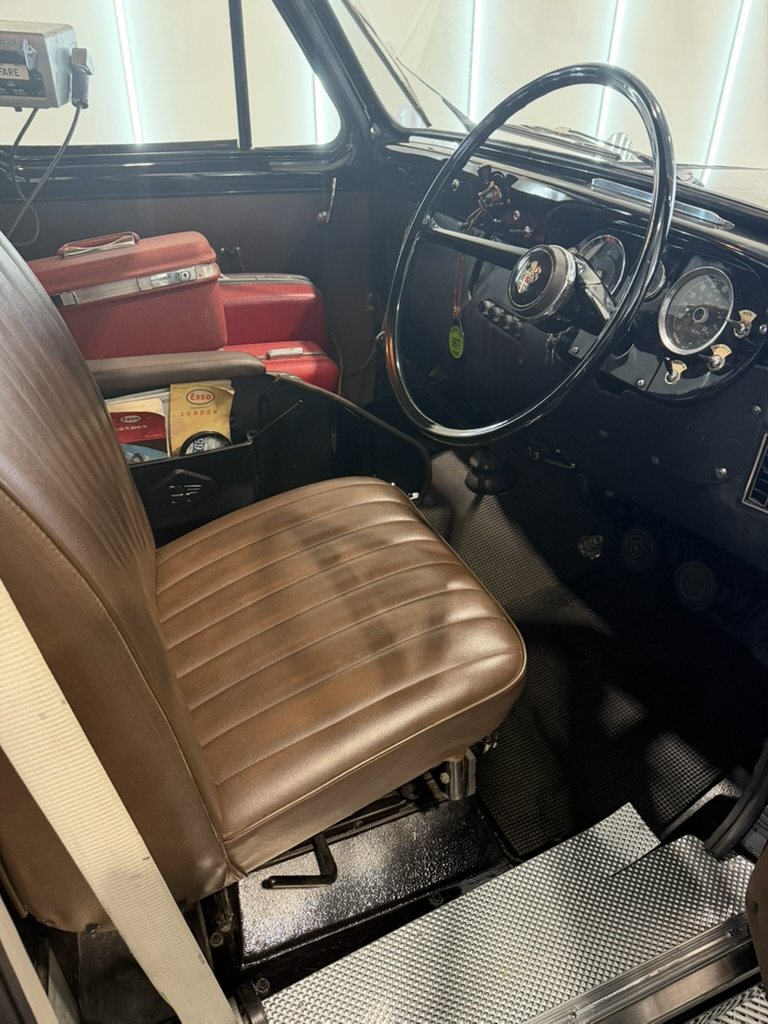 The driver's compartment, a brown leather driver's seat, thin rimmed steering wheel and round gauges, with red vintage suitcases on the platform beside it.