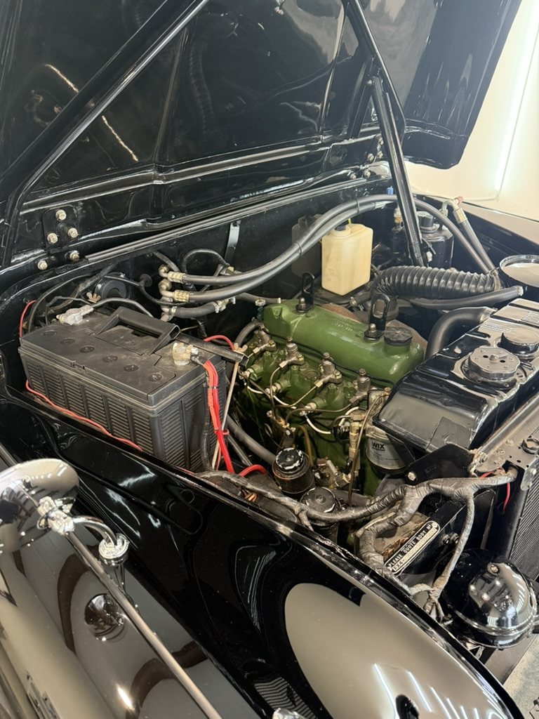 The open bonnet showing the diesel engine painted Austin green, a battery, clean hoses and polished black bodywork around the engine bay.