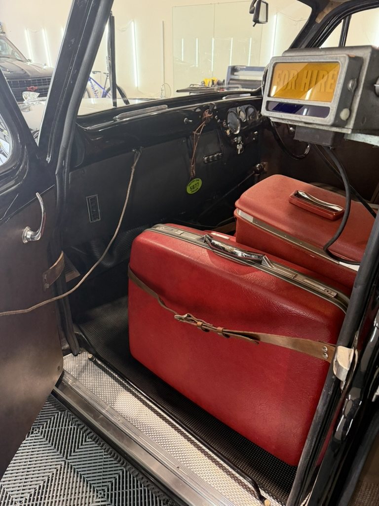 Two red vintage suitcases strapped on the luggage platform beside the driver, with the taximeter mounted above the dashboard.